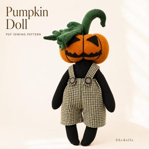 Op de afbeelding: Een stoffen pop met een geribbelde oranje pompoenkop met een zwart gestikt jack-o'-lantern gezicht en een groene steel met bladeren. De pop draagt zwarte lange mouwen en een groen-witte geruite tuinbroek met twee knopen. Tekst: Pumpkin Doll PDF SEWING PATTERN.