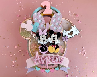 Könnte beinhalten: Ein rosa und blauer Kuchentopper zum Thema Mickey Mouse und Minnie Mouse mit einer Nummer 2, Glitzer und dem Namen Aspen.