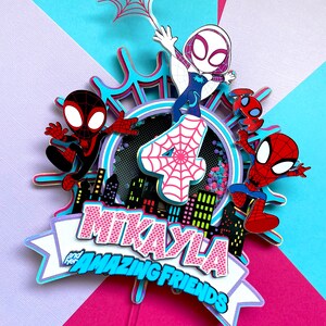 May include: A pink and blue cake topper featuring Spider-Man characters. The topper includes a pink number 4, a white Spider-Gwen figure, and a banner that reads "Mikayla and her Amazing Friends".