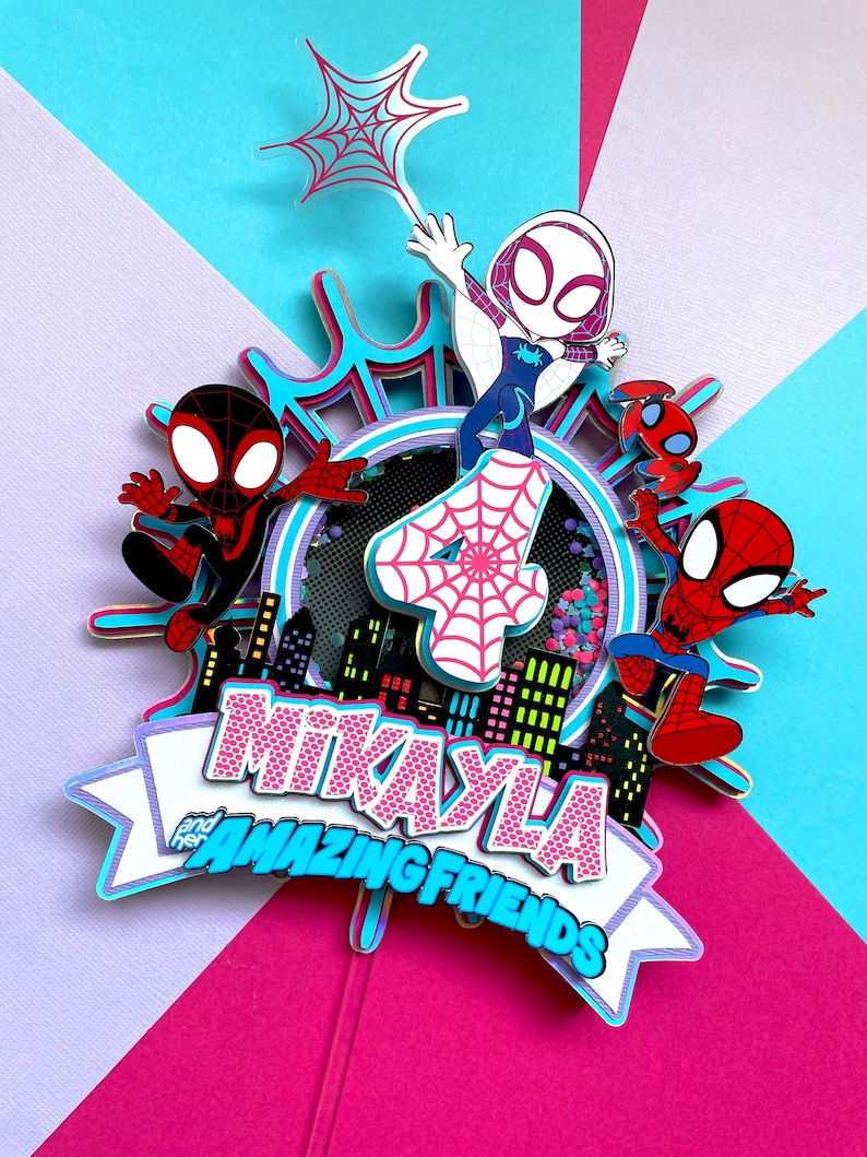 May include: A pink and blue cake topper featuring Spider-Man characters. The topper includes a pink number 4, a white Spider-Gwen figure, and a banner that reads "Mikayla and her Amazing Friends".