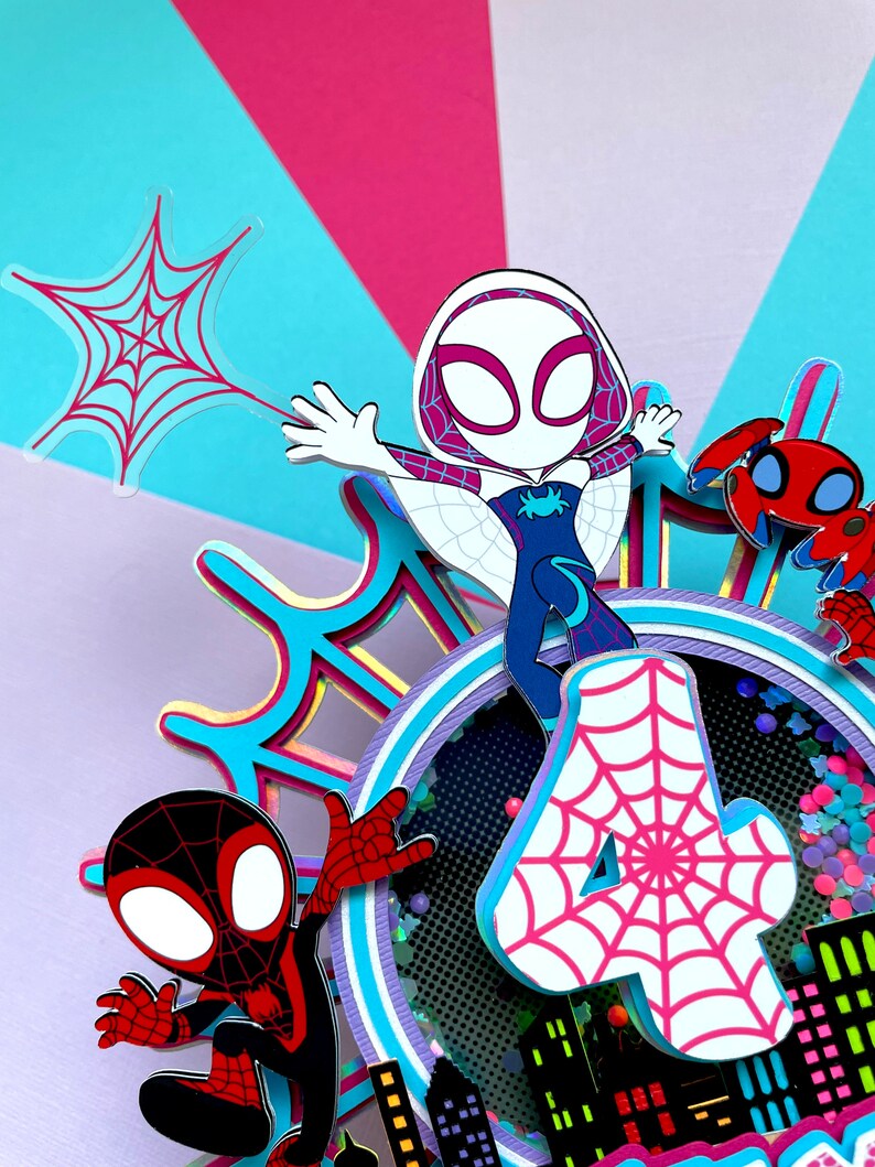May include: A colourful cake topper featuring Spider-Man and Spider-Gwen characters. The topper includes a pink number 4 with a white spiderweb design, a red and black Spider-Man figure, a white Spider-Gwen figure, and a red spider. The topper is ideal for a Spider-Man themed birthday party.