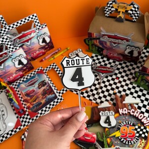 Pode incluir: Um conjunto de decora&ccedil;&atilde;o de festa tem&aacute;tica de Cars com um padr&atilde;o de xadrez preto e branco. O conjunto inclui uma placa que diz "Rota 4", uma placa que diz "Ka-Chow!" com um raio e o n&uacute;mero 95, e uma placa que diz "Leonardo" com um gr&aacute;fico de carro vermelho.