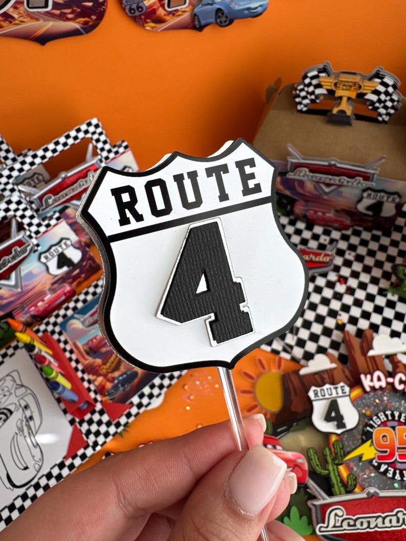 Pode incluir: Topper de bolo branco e preto com uma placa branca que diz "ROUTE 4" em texto preto. A placa tem a forma de uma placa de estrada cl&aacute;ssica.