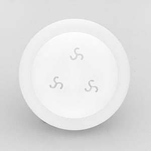 May include: A white, circular object with a raised edge and three stylized, curved symbols evenly spaced in the center. The object appears to be made of a smooth, matte material.