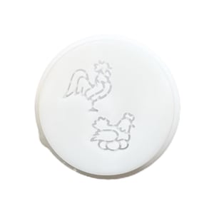 Puede incluir: Una tapa de cerámica blanca y circular con un diseño de gallo y gallina grabado en la superficie. El gallo está de pie y la gallina está sentada sobre huevos. El diseño es de color gris claro.