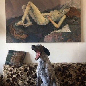 May include: A gray and white dog with black ears yawns while sitting on a floral patterned couch. A painting of a nude woman lying down is hanging on the wall behind the dog.