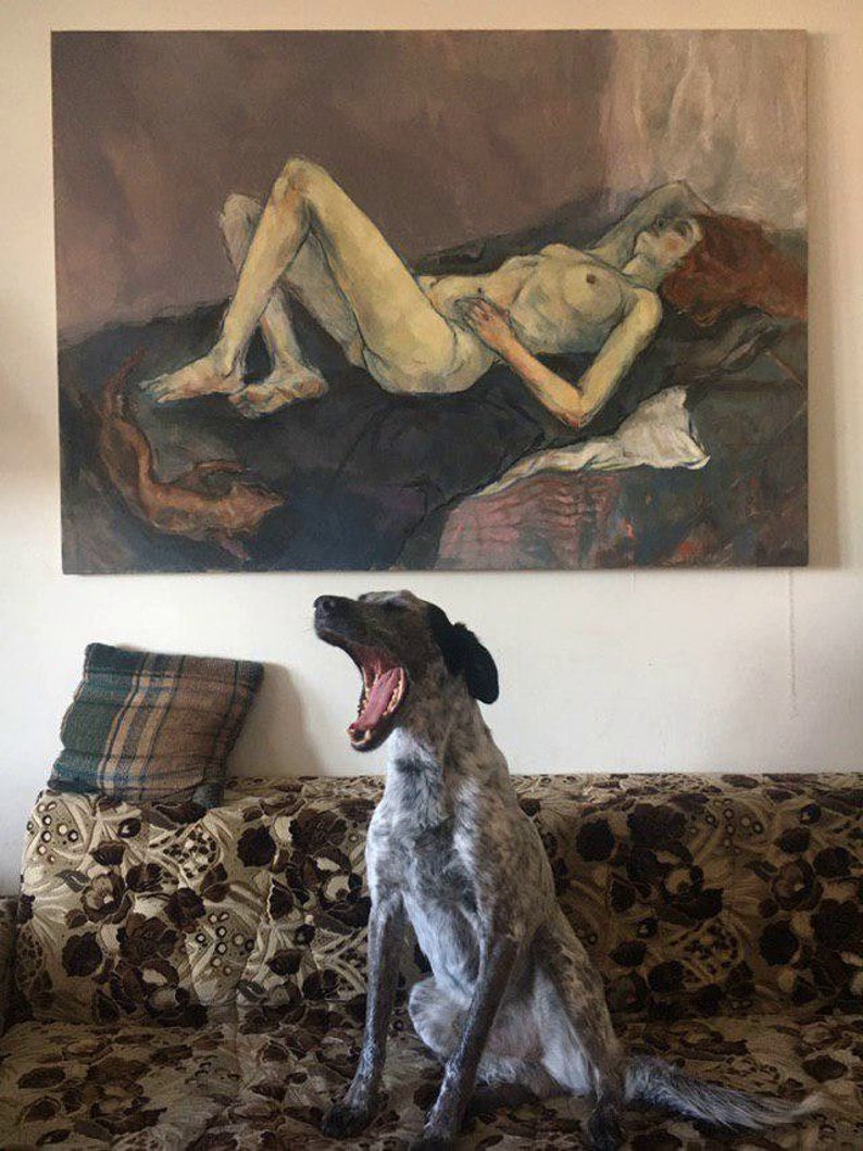 May include: A gray and white dog with black ears yawns while sitting on a floral patterned couch. A painting of a nude woman lying down is hanging on the wall behind the dog.