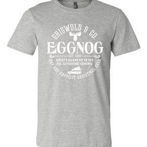 May include: Gray t-shirt with a white graphic design that says "Griswold & Co. Eggnog Est. 1989" with a moose and a car with a Christmas tree on top. The text around the graphic says "Hap, Hap, Happiest Christmas Ever."