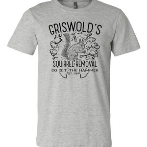 May include: A gray t-shirt with a black and white illustration of a squirrel in a tree. The text "Griswold's Squirrel Removal Go Get The Hammer Est. 1989" is printed on the shirt.