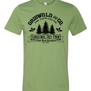 May include: Green t-shirt with a black graphic of a Christmas tree farm called "Griswold and Co." with the text "Little Full Lotta Sap" and "A Real Beaut Guaranteed Est. 1989".