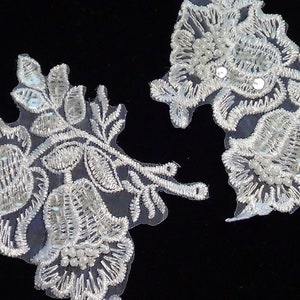 May include: Two white lace appliques with pearl and sequin embellishments. The appliques feature floral designs with delicate leaves and intricate details.