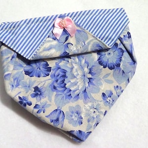 May include: A small, folded fabric pouch with a floral pattern in shades of blue and white. The flap is striped blue and white, and a small pink bow adorns the top. The pouch is likely used for small items.
