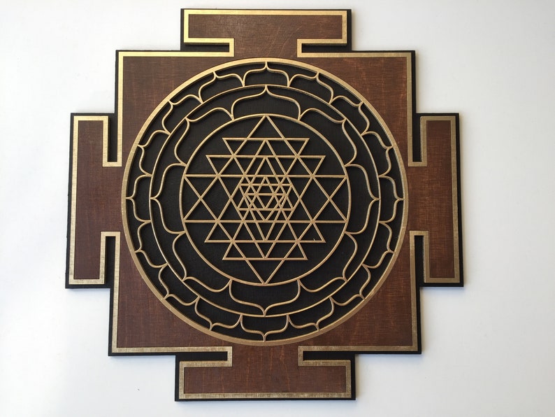 May include: A wooden wall art piece featuring a geometric Sri Yantra design. The artwork has a dark brown background with gold and black accents. The central design is a complex arrangement of triangles and circles.