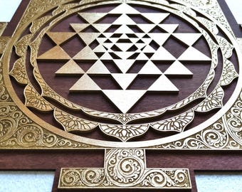 May include: A wooden wall art piece featuring a gold-colored Sri Yantra design. The geometric pattern is set against a dark brown background, with intricate floral and swirl carvings around the edges.