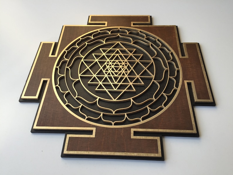 May include: A wooden wall art piece featuring a layered geometric design. The artwork has a dark brown base with gold and black accents. The central design is a gold-colored Sri Yantra symbol.