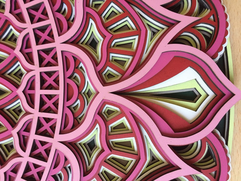 K&ouml;nnte beinhalten: Ein mehrschichtiges Kunstwerk mit einem floralen oder Mandala-Muster. Das Kunstwerk verwendet Schattierungen von Rosa, Rot, Wei&szlig; und Gelb und erzeugt einen komplexen, strukturierten Effekt. Es scheint aus geschnittenem Papier oder Holz zu bestehen, mit einem dreidimensionalen Aussehen.