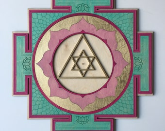 May include: A wooden wall hanging with a geometric design in shades of pink, teal, and gold. The design features a central triangle with a star inside, surrounded by a circle of lotus flowers.