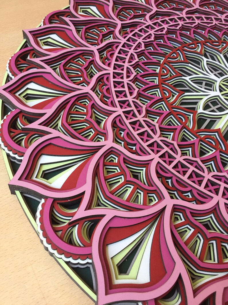 K&ouml;nnte beinhalten: Ein mehrschichtiges, kreisf&ouml;rmiges Mandala-Kunstwerk. Das Design zeigt komplizierte Blumenmuster in Rosa, Rot, Wei&szlig; und Schwarz. Das Kunstwerk besteht aus mehreren Schichten, wodurch ein 3D-Effekt entsteht.