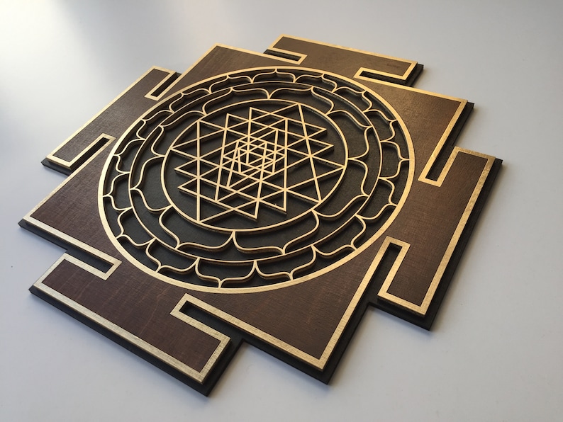 May include: A wooden wall art piece featuring a layered geometric design. The artwork has a dark brown base with gold accents and a central gold geometric pattern. The design is a square with a circular pattern in the center.