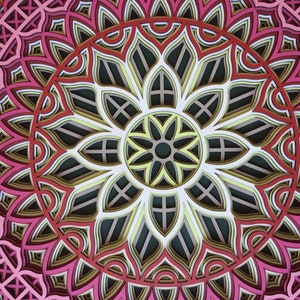 K&ouml;nnte beinhalten: Ein mehrschichtiges Papierkunstwerk mit einem symmetrischen floralen Design. Das Kunstwerk zeigt ein Mandala-&auml;hnliches Muster mit konzentrischen Kreisen in Rosa-, Rot-, Gelb- und Gr&uuml;nt&ouml;nen. Das komplizierte Design stellt eine Blume dar.