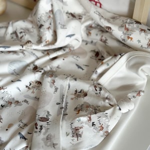 Può includere: Una coperta per neonati bianca e un cappello annodato abbinato con un design a mappa del mondo. La mappa presenta animali ed etichette geografiche in marrone e grigio. La coperta e il cappello sono in tessuto morbido.