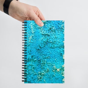 May include: A blue and white spiral notebook with a textured cover. The cover has a pattern of small, irregular shapes.