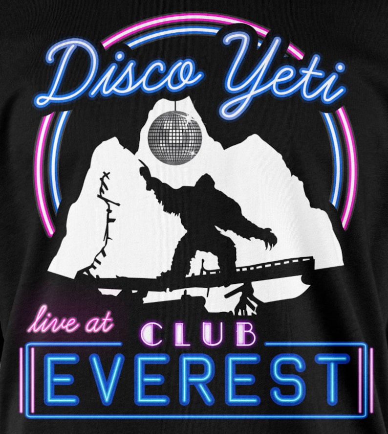 Op de afbeelding: Een zwart T-shirt met een witte afbeelding van een yeti die een discobal vasthoudt. De tekst "Disco Yeti" staat in een neonblauwe en roze lettertype boven de yeti. De tekst "live at CLUB EVEREST" staat in een neonblauw lettertype onder de yeti.