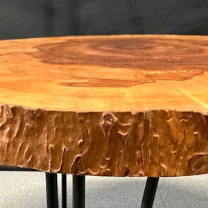 Peut inclure: Une table basse ronde en bois avec une finition en bois naturel et un bord brut. La table a des pieds en épingle à cheveux noirs.