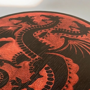 Peut inclure: Une table ronde en bois avec une finition noire et un motif de dragon rouge. La table a un piétement métallique avec deux pieds.