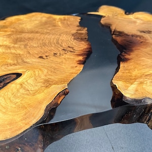 Könnte beinhalten: Eine Tischplatte aus Holz mit einer natürlichen Holzmaserung und einer schwarzen Epoxidharzeinlage. Die Tischplatte ist unregelmäßig geformt und hat eine Live-Kante.