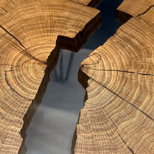 Op de afbeelding: Close-up van een houten tafelblad met een natuurlijke rand en een scheur die is gevuld met helder hars. De houtnerf is zichtbaar en het hars is glad en glanzend.