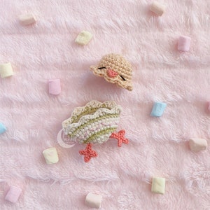 May include: A crocheted chick with a yellow hat and green and white body. The chick is sitting on a pink fuzzy surface.