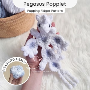 Könnte beinhalten: Ein weiß-hellblaues, gehäkeltes Pegasus Poppet Fidget-Spielzeug mit Flügeln und einem langen Schwanz. Der Text Pegasus Poppet Popping Fidget Pattern ist oben sichtbar, und ein kreisförmiger Einsatz zeigt das Spielzeug als Kugel mit dem Text ROLLS INTO A BALL.
