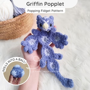 Może przedstawiać: Szydełkowa zabawka typu fidget griffin poppet w kolorze fioletowym i jasnoniebieskim o teksturowanej powierzchni z włóczki. Zabawka posiada głowę, skrzydła i długi ogon oraz okrągłą wstawkę pokazującą zabawkę zwiniętą w kulkę z napisem ROLLS INTO A BALL.