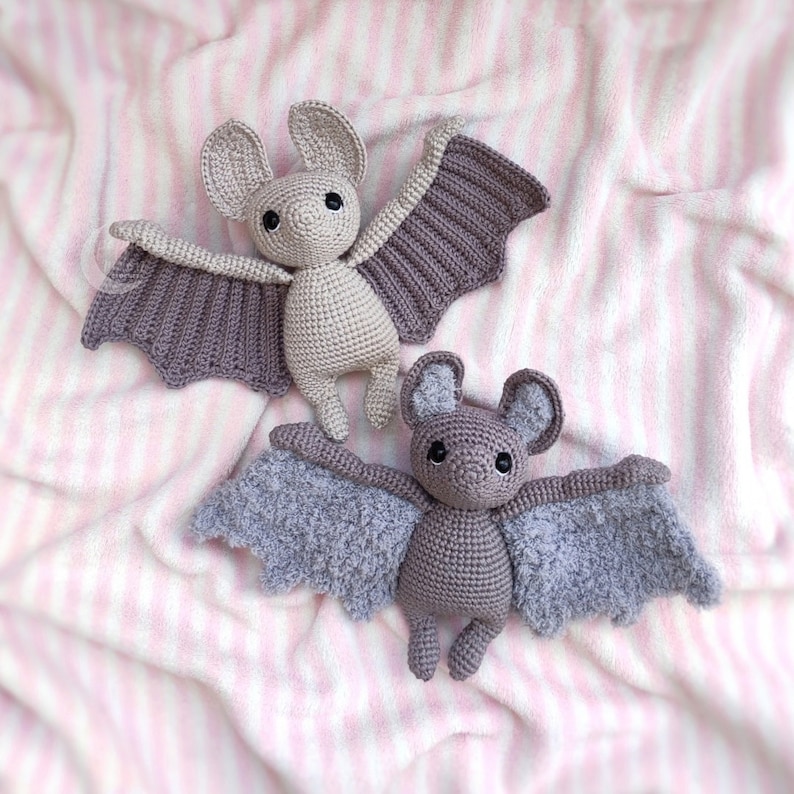 May include: Two crocheted bat toys. One bat is gray with a fuzzy texture and the other bat is purple with a smooth texture.