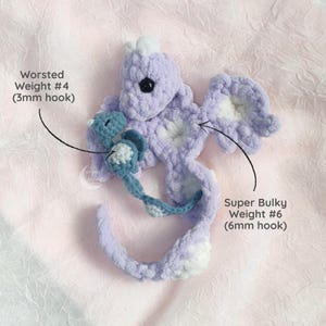 May include: A handmade crochet seahorse in shades of lavender and white, with a smaller blue seahorse attached. The text indicates the use of Worsted Weight #4 yarn with a 3mm hook and Super Bulky Weight #6 yarn with a 6mm hook.