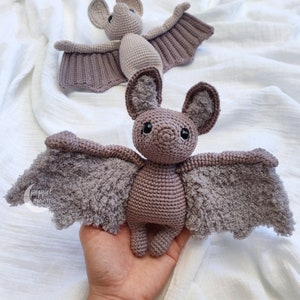 May include: A crocheted purple bat with fuzzy wings. The bat has black eyes and a small, pointed nose.
