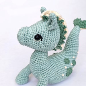 May include: A crocheted seahorse toy with a green body, white and green mane, and black eyes. The seahorse has a white belly and green spots on its back.