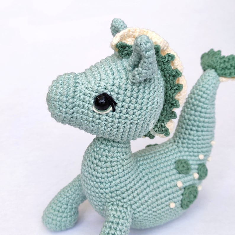 May include: A crocheted seahorse toy with a green body, white and green mane, and black eyes. The seahorse has a white belly and green spots on its back.