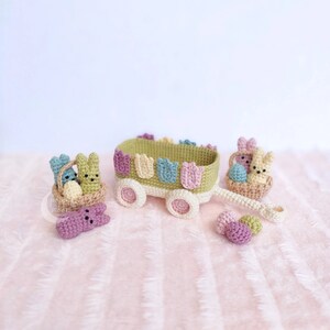 May include: A green and white wagon with a basket of pastel colored Easter eggs and bunnies. The wagon has a handle and wheels. There are three pastel colored eggs on the ground.