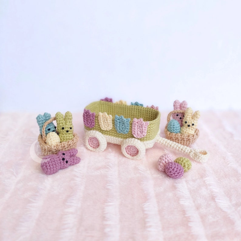 May include: A green and white wagon with a basket of pastel colored Easter eggs and bunnies. The wagon has a handle and wheels. There are three pastel colored eggs on the ground.