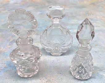 Precioso juego de tres frascos de perfume vintage de cristal transparente con tapones.