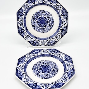 May include: Two octagonal ceramic plates with white and blue floral patterns. The plates feature a central floral design and a detailed border, showcasing a classic, elegant aesthetic. The plates are displayed on clear stands, reflecting a traditional style.