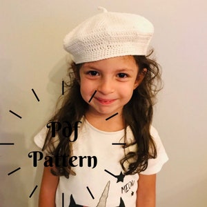 Peut inclure: Un béret blanc en crochet avec un motif de point simple. Le béret est porté par un enfant aux longs cheveux bruns. Le texte "Pdf Pattern" est écrit en noir sur fond blanc.