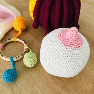 Peut inclure: Un ensemble de jouets pour b&eacute;b&eacute; en crochet, comprenant un hochet avec un anneau en bois, une balle blanche avec un cercle rose et une pieuvre multicolore. Les jouets sont sur une surface en bois.
