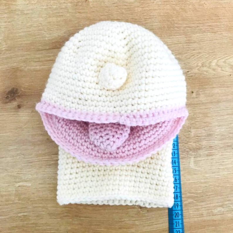 Peut inclure: Chapeau &agrave; capuche en crochet blanc avec une bordure en crochet rose et un petit pompon blanc sur le dessus.