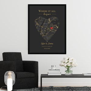 May include: A black and gold framed print with a heart-shaped map of a city. The map is outlined in gold and has a red heart in the center. The text "Where it all began" is at the top of the print, and the names "Tyler & Emma" and a date are at the bottom.