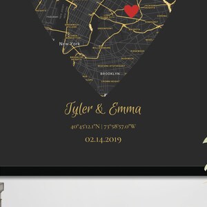 May include: A black and gold map of New York City in the shape of a heart with a red heart marking a location. The text "Tyler & Emma" is written in gold script below the map, along with the coordinates "40&deg;45'12.1"N | 73&deg;58'57.0"W" and the date "02.14.2019".
