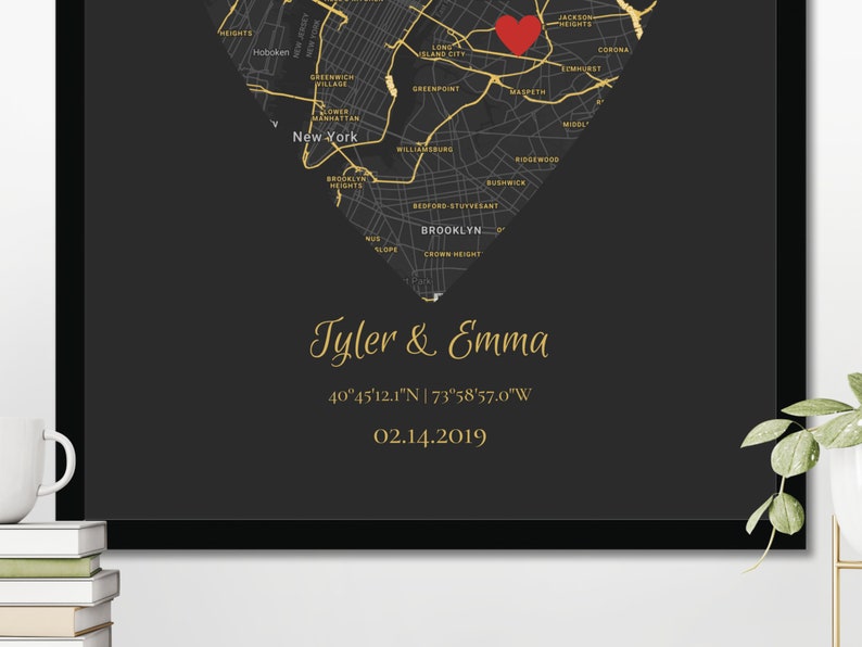 May include: A black and gold map of New York City in the shape of a heart with a red heart marking a location. The text "Tyler & Emma" is written in gold script below the map, along with the coordinates "40&deg;45'12.1"N | 73&deg;58'57.0"W" and the date "02.14.2019".