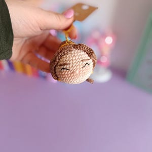 May include: A crocheted doll with brown hair and a smiling face. The doll is made of yarn and has a simple design.
